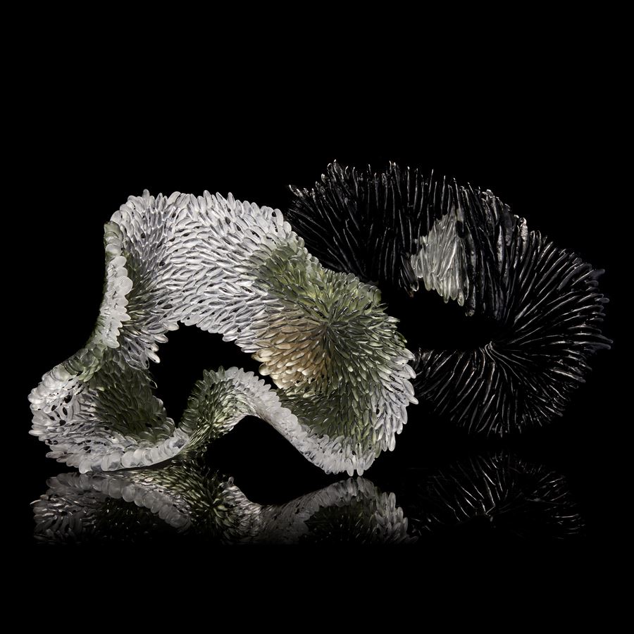 clear textured organically looped standing glass sculpture with one side scaled the other smooth with areas in clear soft moss green and bronze with speckles and dots of opaque black